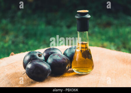 Acquavite di prugne (Slivovitz) in serbo tradizionale bottiglia di vetro con fresche susine mature su una superficie di legno. Foto Stock