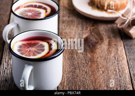 Frutta calda tè con le fette di limone in bianco rustico mug sul tavolo di legno, intime calda bevanda invernale Foto Stock