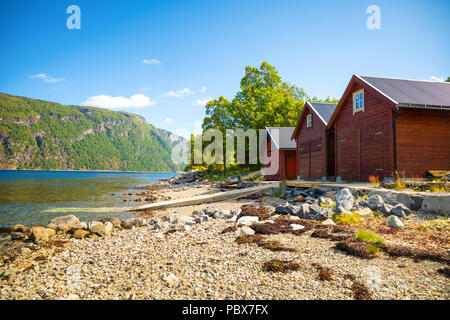 Tipico legno norvegese rorbu capanna sulla spiaggia del fiordo nella soleggiata giornata estiva in Norvegia Foto Stock