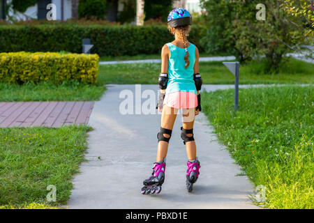 Vista posteriore della bambina nel casco blu e colorati vestiti sport su pattini a rotelle Foto Stock