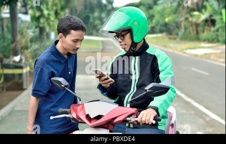 Giovane uomo motociclo taxi driver controllo ordine passeggero prima di corsa Foto Stock