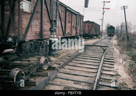 Immagine stilizzata vintage stazione ferroviaria con carri sui binari e pali del telegrafo in un giorno nuvoloso Foto Stock