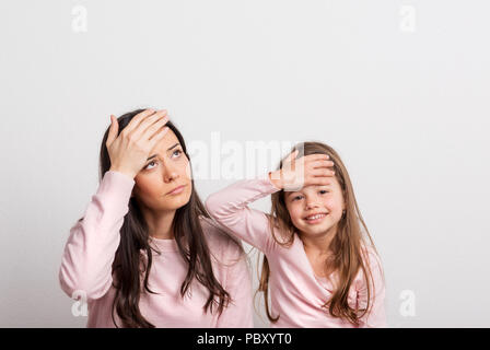 Una piccola ragazza e sua madre in un monolocale, mani sulla loro fronte. Foto Stock