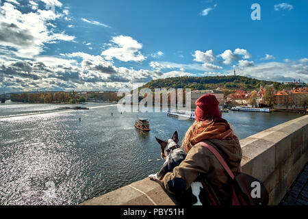 Giovani donne turistico con un cucciolo di cane e uno zaino guardando l'imbarcazione turistica e cigni vela sul fiume Moldava dal Ponte Carlo (Karluv la maggior parte Foto Stock