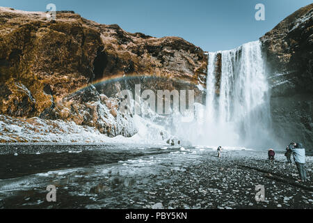 Skogafoss cascata in Islanda con arcobaleno su una giornata soleggiata con cielo blu. Foto Stock