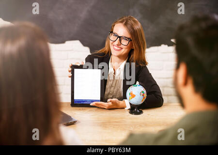 Bellissima femmina agente di viaggio in bicchieri sta dando i suoi clienti biglietti e documenti, tutti sono sorridente Foto Stock