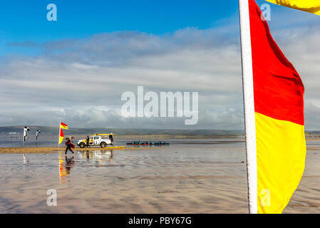 Surfers e marker di sicurezza bandiere sulla spiaggia di Condino, Devon, Regno Unito Foto Stock