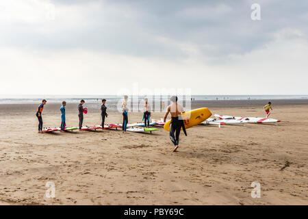Surfers preparando le loro commissioni accanto al surf e sci racing Canoe sulla spiaggia di Condino, Devon, Regno Unito Foto Stock