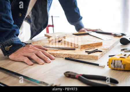 Carpenter operando con cautela guardando i piani di lavoro in falegnameria. Egli è imprenditore di successo al suo posto di lavoro. martellare un chiodo supporta sulla build Foto Stock
