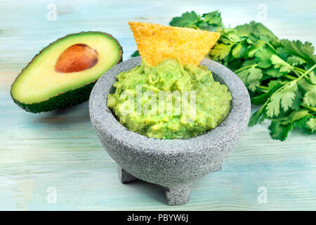 Una foto di salsa guacamole in un molcajete, tradizionale mortaio messicano, con un nacho chip, il coriandolo, e avocado, su teal Foto Stock