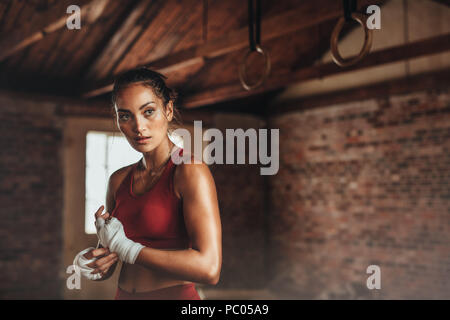 Certi giovani femmine boxer cinturino da indossare sul polso. Il pugilato pratica presso la palestra. Donna in abbigliamento sportivo la preparazione per la boxe lotta o allenamento. Foto Stock