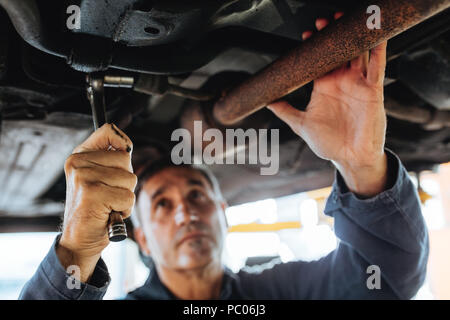 Auto serraggio meccanico del sistema di scarico del tubo sotto l'auto. Riparazione auto di uomini che fissa un auto in una stazione di servizio. La messa a fuoco in repairman mano con spanne chiave Foto Stock