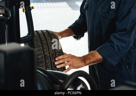 Tagliate il colpo di un meccanico di controllo della condizione di una ruota di automobile. Uomo di esaminare il grado di usura dei pneumatici per auto in garage. Foto Stock
