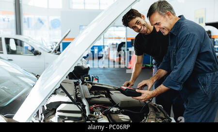 Due lieti automobile meccanica facendo auto motore checkup con un dispositivo. Meccanica la diagnosi di un'auto in una stazione di servizio. Foto Stock