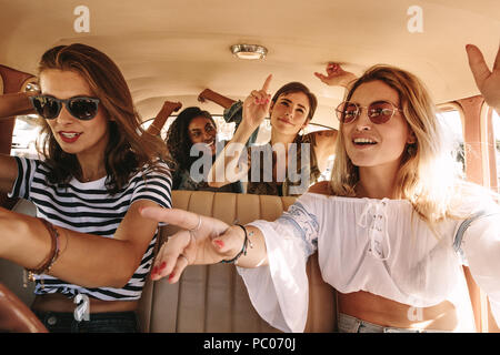 Un gruppo di giovani donne di cantare e ballare in auto in un viaggio su strada. Multirazziale amiche divertirsi su una vettura da corsa. Foto Stock