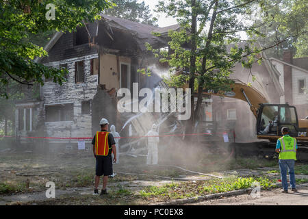 Detroit, Michigan - Polvere avvolge un cantiere come lavoratori, utilizzando abbigliamento protettivo per la protezione contro l'esposizione all'amianto, demolire una casa abbandonata. Un