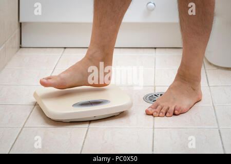 Immagine ritagliata dell'uomo piedi intensificazione su bilance, sul pavimento del bagno Foto Stock