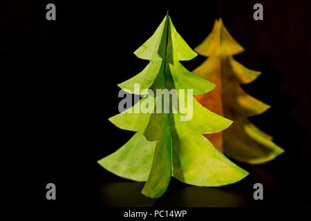 Albero di natale miniatura su uno sfondo scuro con spazio copia.Origami albero di Natale con il libro verde isolato su sfondo scuro per la decorazione, vista frontale. Flat Top laici visualizzare la minima nozione di vacanza. Foto Stock