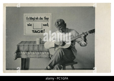 German Historical photo Cartolina: soldato nel tappo di foraggio suona la chitarra seduto su una sedia. L'esercito di svago, seconda guerra mondiale, la Germania, il Terzo Reich Foto Stock