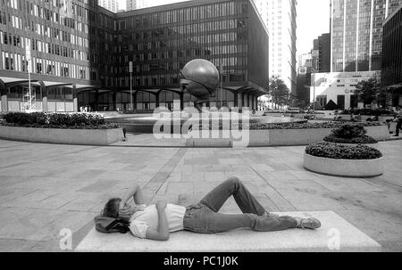 Manhattan, 1982. Uomo appoggiato nel World Trade Center Plaza. La sfera della scultura e la fontana nel WTC Plaza. Foto Stock