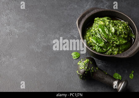 Pesto di basilico con salsa di formaggio parmigiano, noci, olio d'oliva e aglio in ghisa nera mortaio, vista ravvicinata Foto Stock