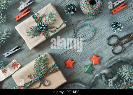 Rustico sfondo di legno in verde e in arancione con rami di abete e i regali di Natale in semplice carta da imballaggio marrone. Stagionale colpo di sfondo da sopra Foto Stock