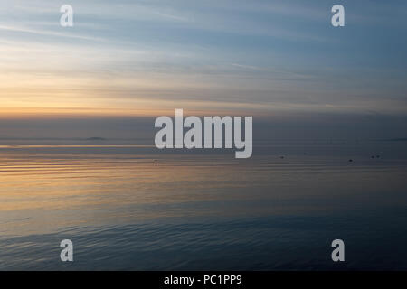 Lago Trasimeno (Umbria) al tramonto, con toni morbidi nel cielo e acqua e bellissimi riflessi dorati Foto Stock