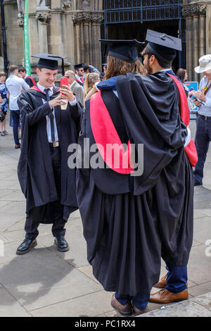 Laureato giovane uomo prendendo fotografia di amici dopo la laurea in Bristol West of England Regno Unito. Indossando le schede di mortaio e gli abiti. Foto Stock