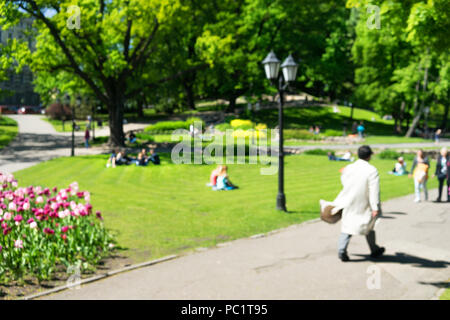 Un uomo in un impermeabile va al parco nella città di Riga su una soleggiata giornata di primavera su uno sfondo di verdi alberi. Sfocata Foto Stock