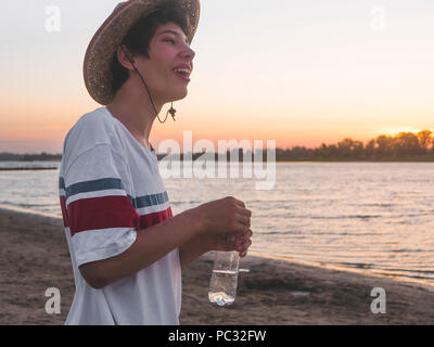 Close up ritratto di giovane adolescente di sesso maschile in casuale e l'estate hat acqua potabile su una spiaggia Foto Stock