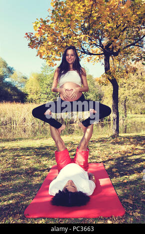 L uomo e la donna incinta facendo acro yoga nel parco. Messa a fuoco selettiva Foto Stock
