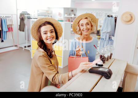 Il pagamento per i vestiti. Trasmissione via IR di donne attraenti sensazione estremamente felice di pagare per i vestiti nuovi Foto Stock