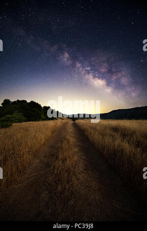 Una strada sterrata che passa attraverso un campo con il cielo notturno, la Via Lattea e stelle overhead vicino lago, Sonoma California. Foto Stock