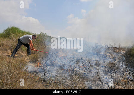 L'uomo cerca di estinguere ancora un altro incendio causato da Kite palestinese bombe che sono state percorse da Gaza con un acceso benzina panno imbevuto per impostare gli incendi per Foto Stock