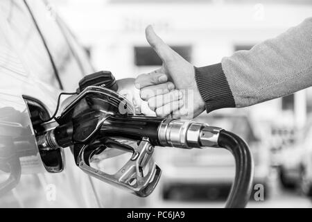 Benzina o gasolio che viene pompato in un veicolo a motore auto. Primo piano dell'uomo, che mostra il pollice fino gesto, pompando benzina in auto alla stazione di gas. Foto Stock