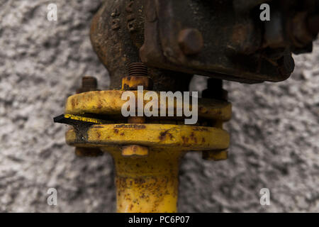 Vecchio weathered gru di gas e il tubo sullo sfondo di un muro grigio. Antico cancello di gas di colore giallo è su un tubo e blocchi di una tubazione. La pipeline con gru per dare gas sulla parete. Foto Stock