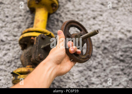 L uomo vecchio di contenimento di gas a spiovente gru sullo sfondo di un muro grigio. Antico cancello di gas di colore giallo è su un tubo e blocchi di una tubazione. La pipeline con gru per dare gas sulla parete. Foto Stock