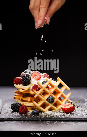 Foto del wafer viennese con lamponi e fragole spolverati con zucchero a velo sulla lavagna contro sfondo bianco Foto Stock