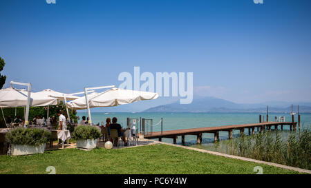 I turisti in un cafe che si affaccia sul bellissimo Lago di Garda e colline pedemontane delle Alpi italiane in una limpida giornata estiva Foto Stock