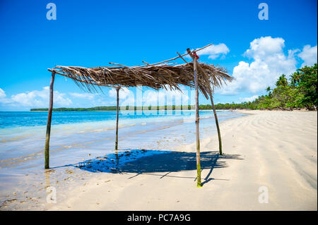 Rustico frond palm e il ramo di albero palapa ombrellone in attesa di ombra ai visitatori di acque poco profonde in una remota orlata di palme spiaggia tropicale del Brasile Foto Stock