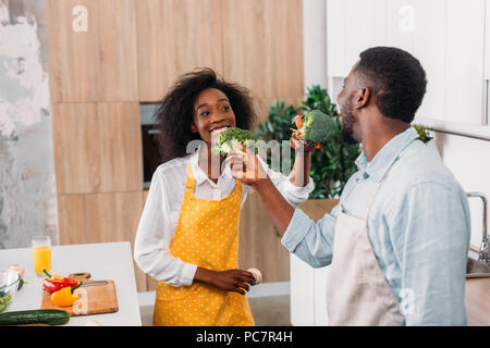 Coppia sorridente divertendosi con broccoli in cucina Foto Stock