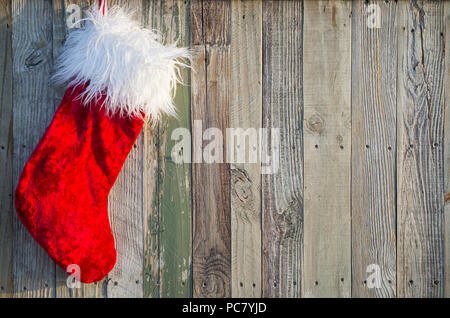 Santa's Christmas Stocking appeso contro un rustico sfondo legno in attesa di essere riempito con i regali di Natale Foto Stock