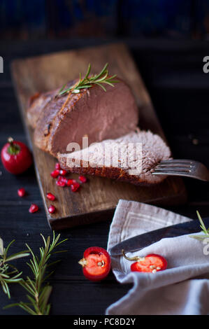 Carni cotte al forno con rosmarino e pepe rosso. Bistecca di manzo. Cena per gli uomini. foto scura. Sfondo nero. pannello di legno Foto Stock