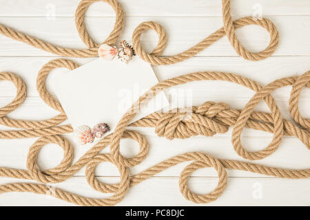 Vista superiore della carta vuoti con conchiglie su marrone Nautica Corde annodate su bianco superficie in legno