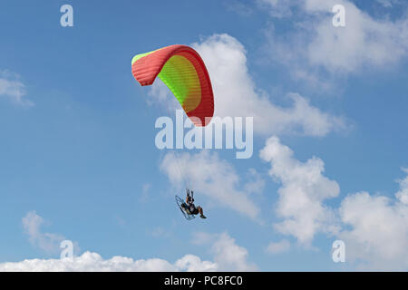 Un powered parapendio volare tra le nuvole contro un cielo blu chiaro Foto Stock