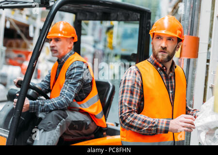 Il lavoratore e il suo anziano collega di lavoro con la macchina di carrello elevatore a forche Foto Stock