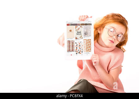 Redhead kid seduto e mostrando caricamento pagina pinterest su tablet isolato su bianco Foto Stock