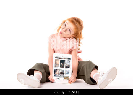 Capelli rossi bambino seduto e azienda tablet con caricata la pagina pinterest su bianco Foto Stock
