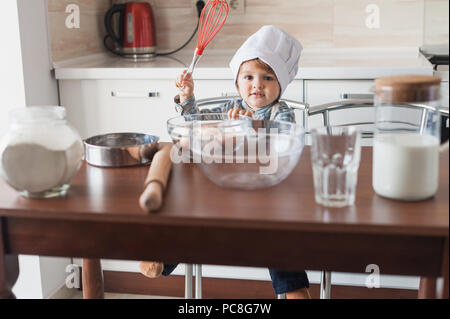 Ragazzino in chef hat holding frusta in mano pronti per cucinare Foto Stock