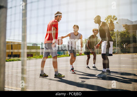 Quattro uomini giocare a basket in un campo di pallacanestro in una giornata di sole. Gli uomini praticano la pallacanestro talento nel dribbling. Foto Stock